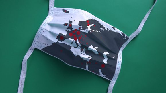 White face mask with a map of Europe is lying on a green background